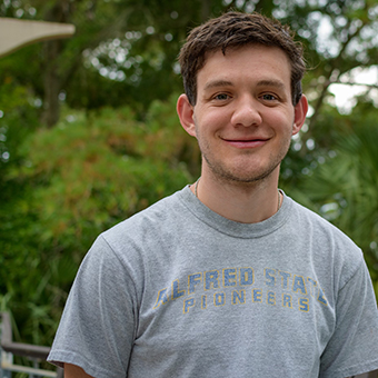 Stephen smiling at the camera with a gray shirt and with greenery in the background