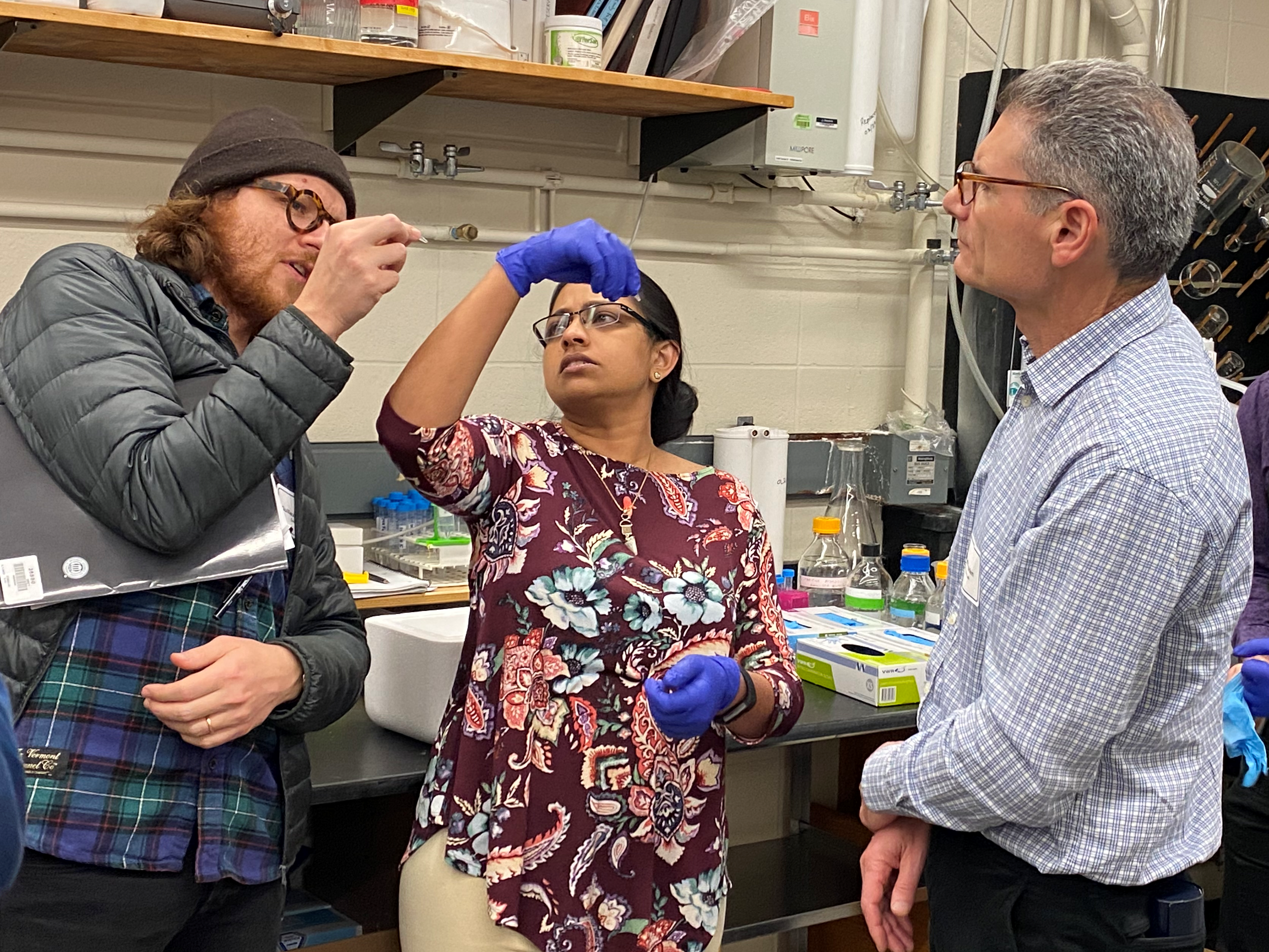 Drs. Duclos, Baskaran and Fraden looking at a liquid container. 