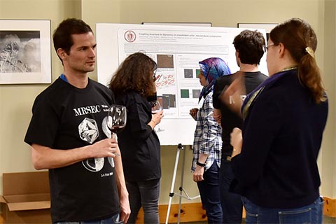 Two students engaged in discussion. In the background are groups of students looking at posters.