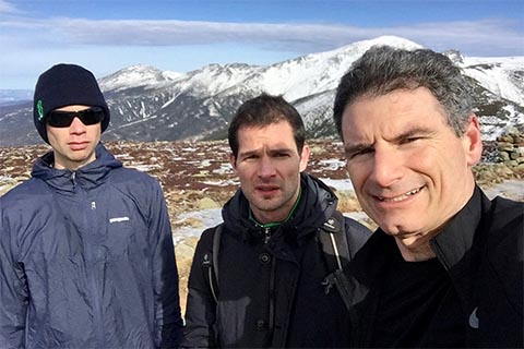 3 participants on a hike pose for a picture in a scenic spot with views of mountains.