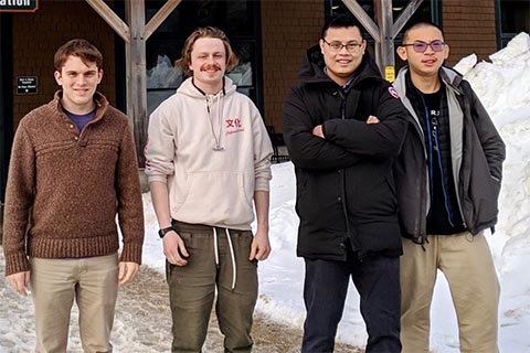 Wu's lab group standing outside in front of a snow bank.