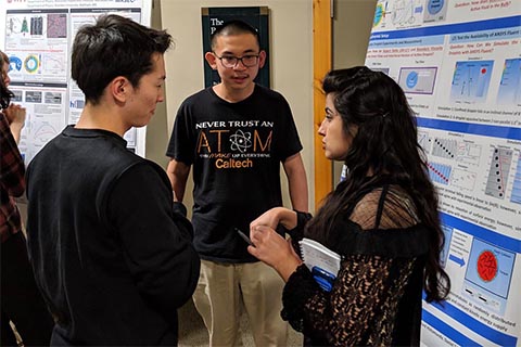 Two men and one woman stand in front of a poster, engaged in discussion.