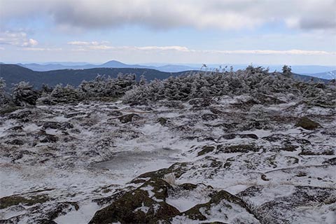 Panoramic view of the mountains from a snow and ice covered rocky summit.