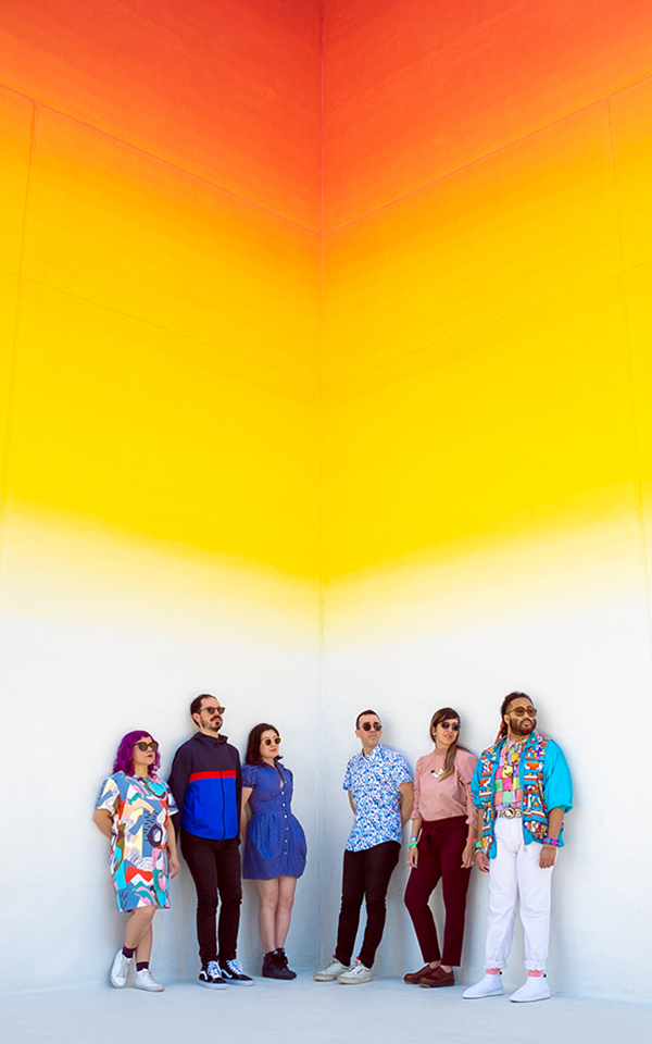 The members of Balún pose in front of a yellow and orange wall