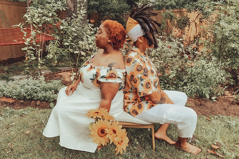 The artists of BOOMscat pose back-to-back in a garden