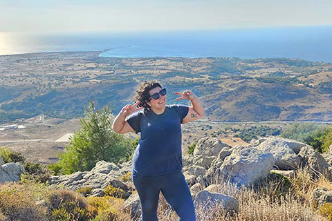 A women stands at the top of a mountain and holds up two peace signs.