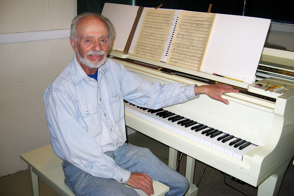 Martin Boykan sits at a white piano