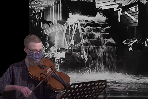 Eric Hollander plays viola in front of a black and white video backdrop of a waterfall