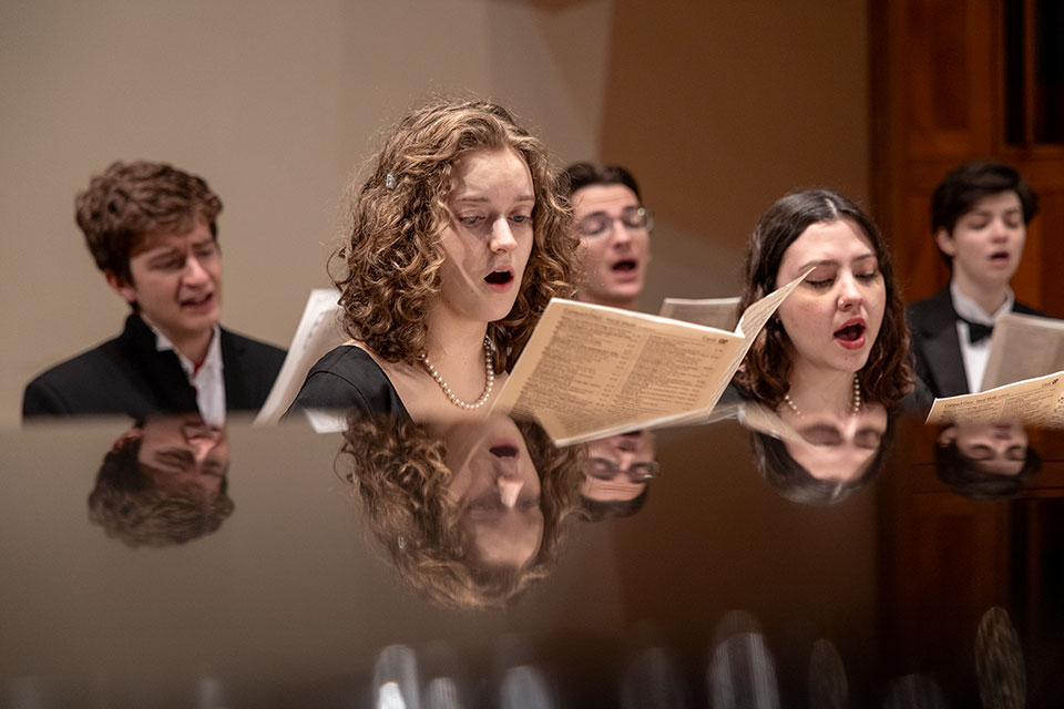 A group of chamber singers sing together on stage.