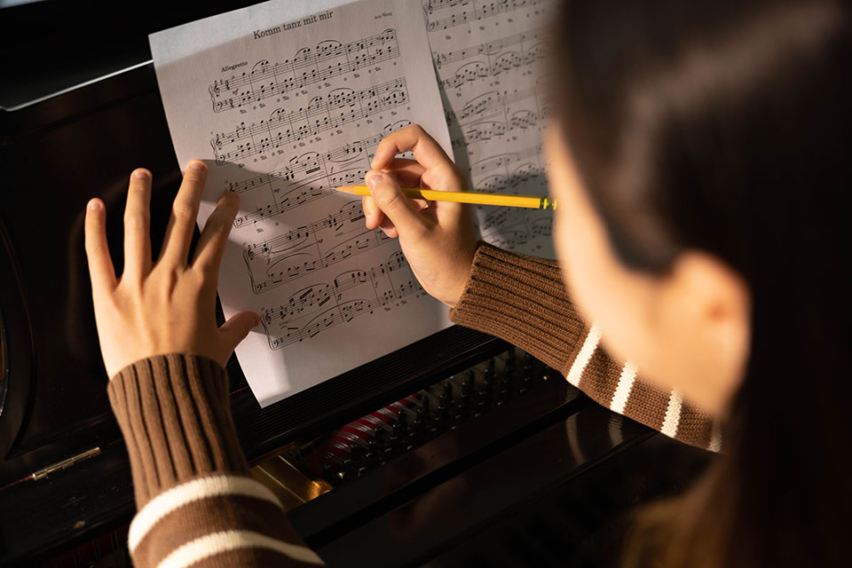 Person writing on a sheet of music while sitting at a piano