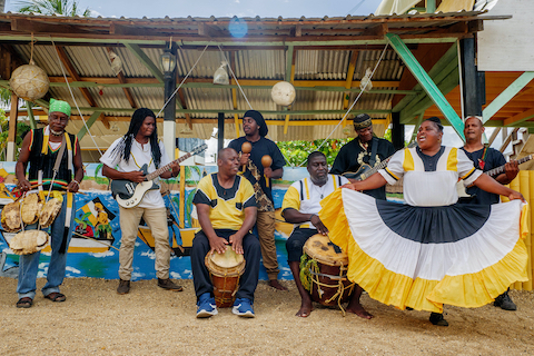 Eight performers in yellow, black and white play music outdoors