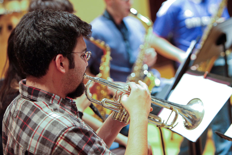 A student plays a trumpet, while other students in the background play saxophone in the background