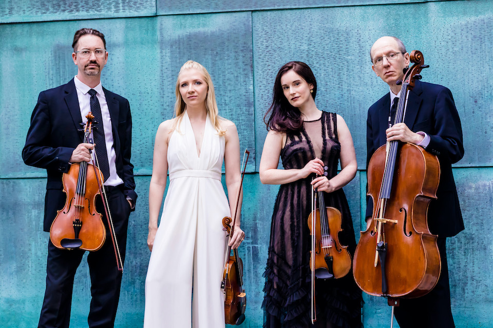 Members of the Lydian String Quartet sit holding their instruments in front of the Shapiro Campus Center