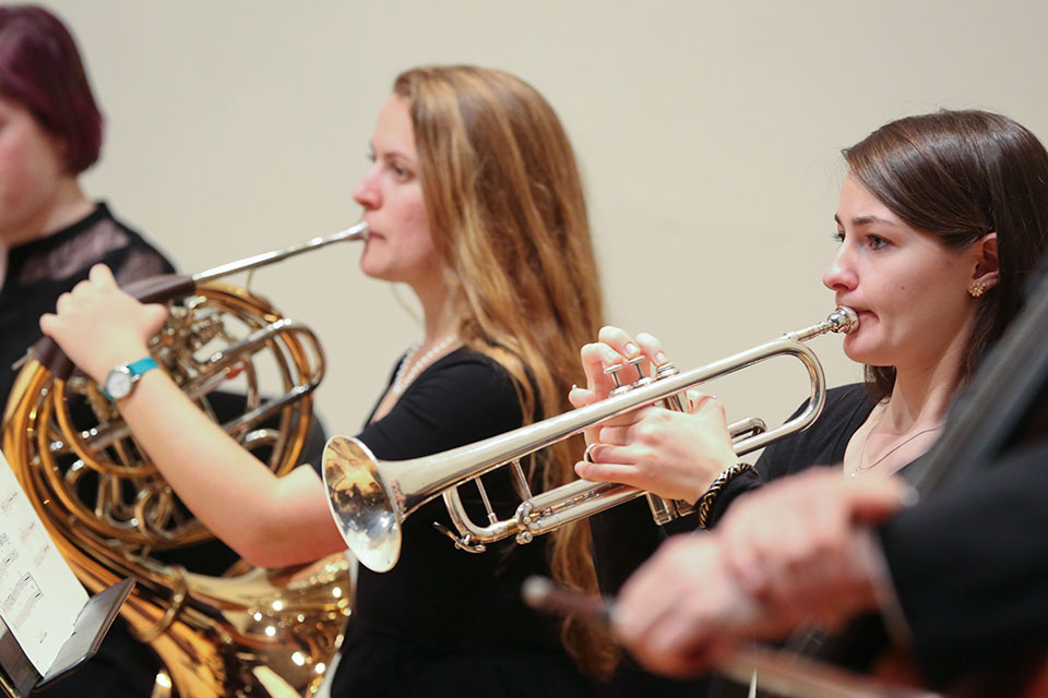 Two students play instruments, one on the trumpet and one on the French Horn