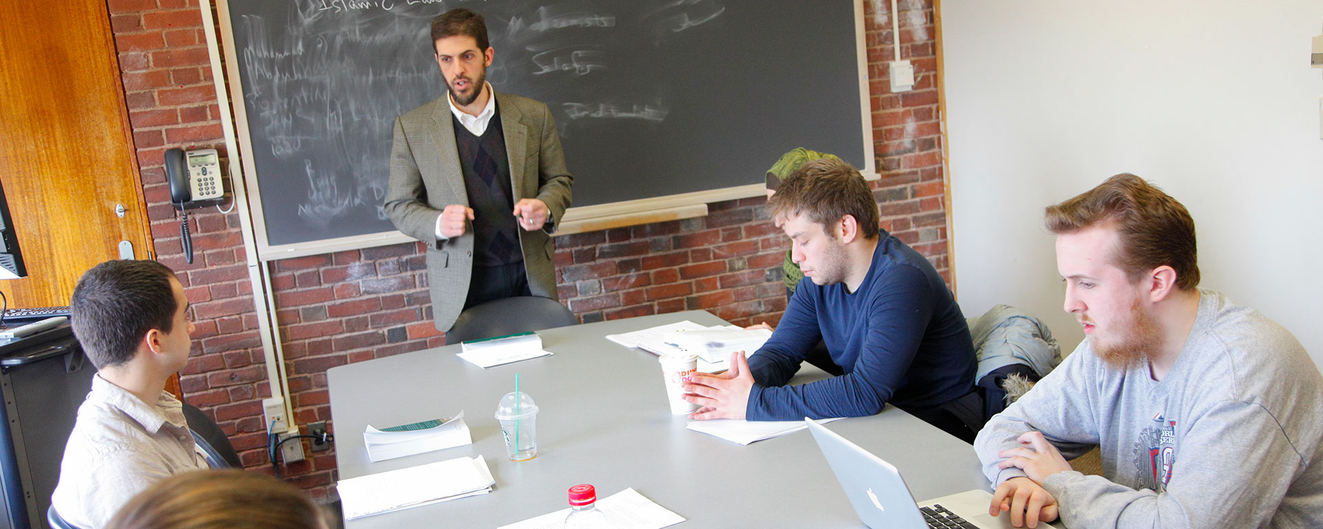 A professor speaks to a small group of students sitting around a table