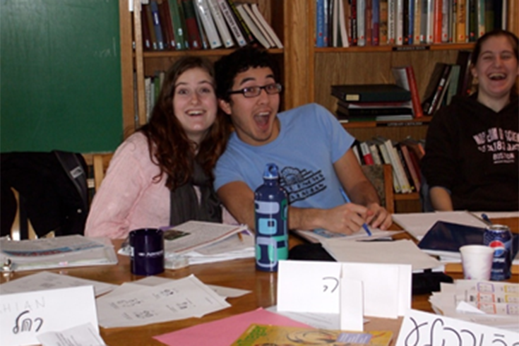 Three people sitting at a table smiling with paper and crafts on the table.