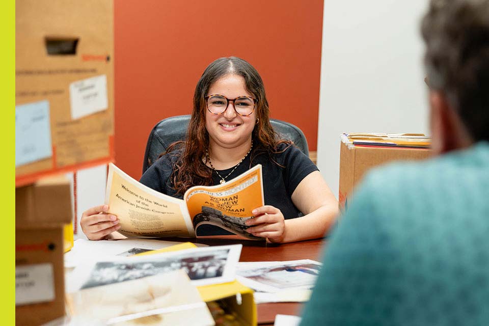 Gabriella works at her internship at the Jewish Women's Archive; materials are seen on the desk in front of her