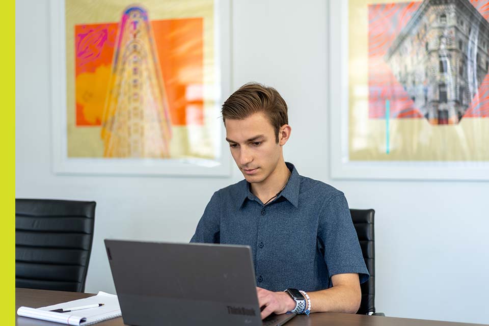 Matthew works at a computer as his internship; artwork appears behind him