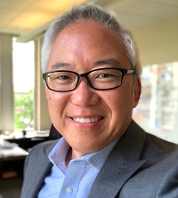 headshot of SVP of Communications, Marketing and External Affairs Dan Kim in blue shirt, sport coat and glasses