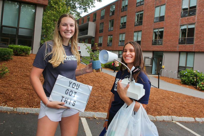 members of the women's volleyball team carry items into a new student's room