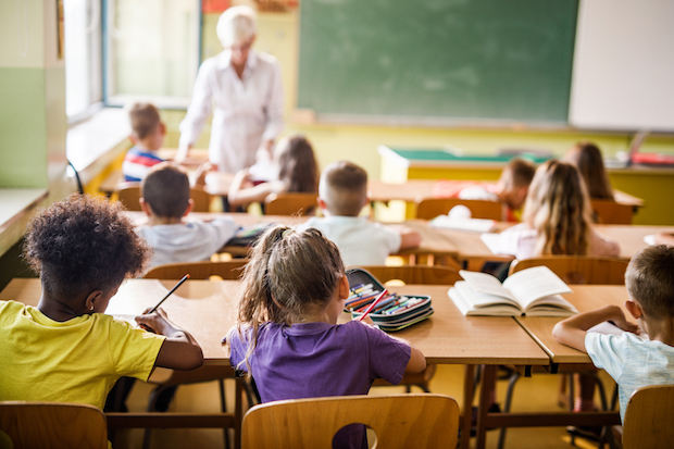 A classroom of young children with the teacher out of focus in the front of the class. Stock image.