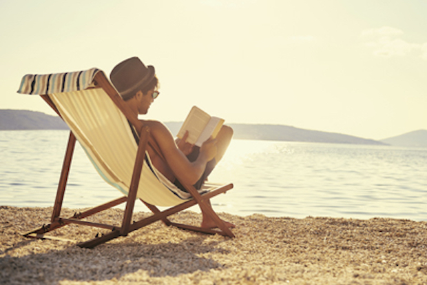 Man sitting in a beach chair reading a book.