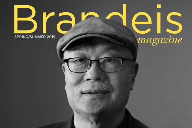 A black and white headshot of alumnus Ha Jin, wearing a cap, in front of the Brandeis magazine logo in yellow