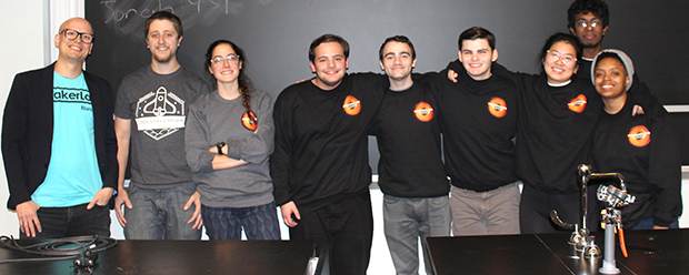 group of people standing against a blackboard and behind a science table