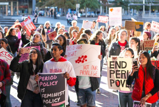 group of young people holding signs promoting menstrual equity at a demonstration