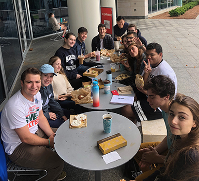 A group of a dozen students sits at round metal tables outside the Shapiro Campus Center