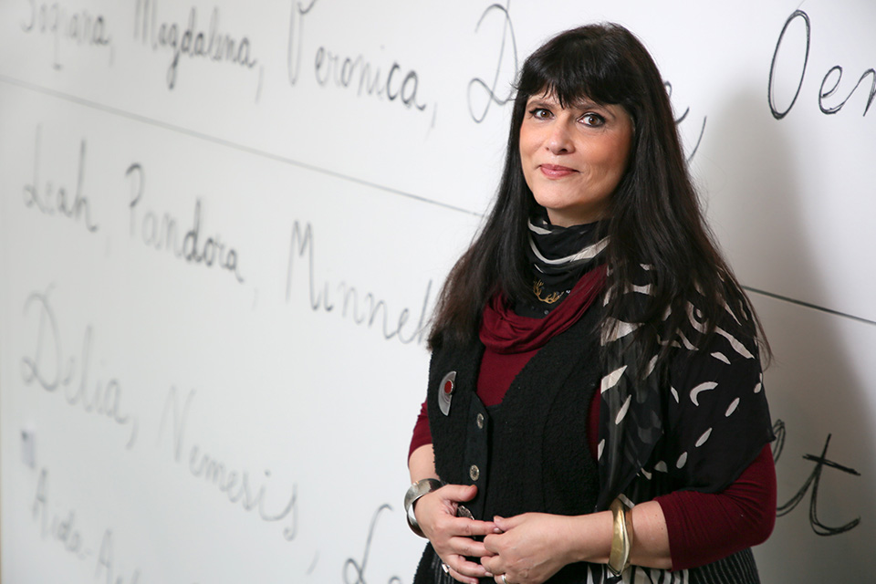 Gannit Ankori stands in front of a wall with large names of women written in charcoal script