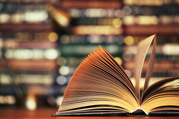 Open book on table, bookshelves in background