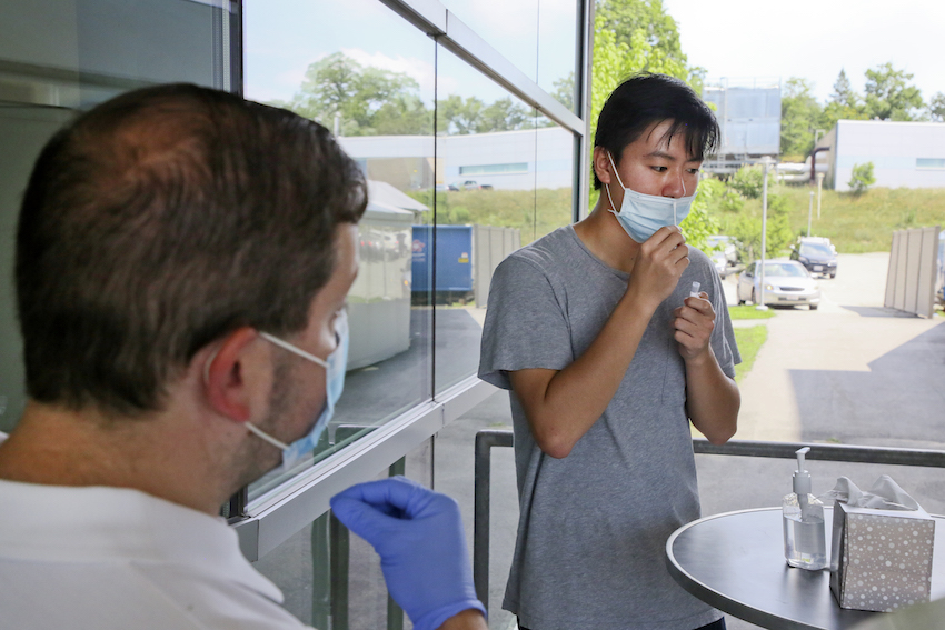 A person self-administers a test while a nurse provides instruction