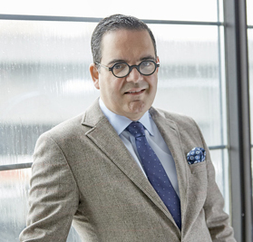 Luis croquer in a suit and tie standing against a window