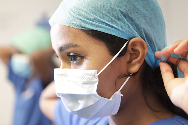 Health worker puts on head covering and wears surgical mask. 