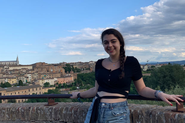 Anya Shire-Plumb standing at a railling with a tuscan town in the distance behind her