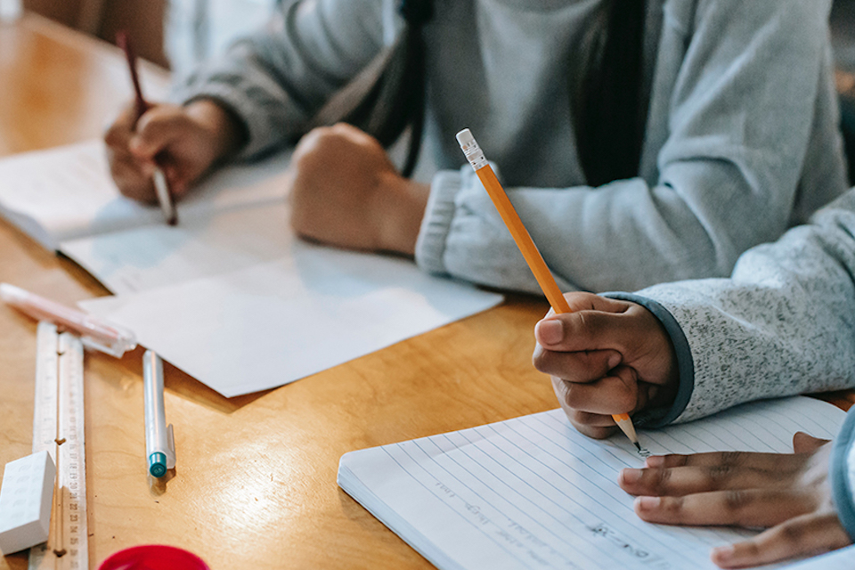 Children's hands, writing on paper on a desk.