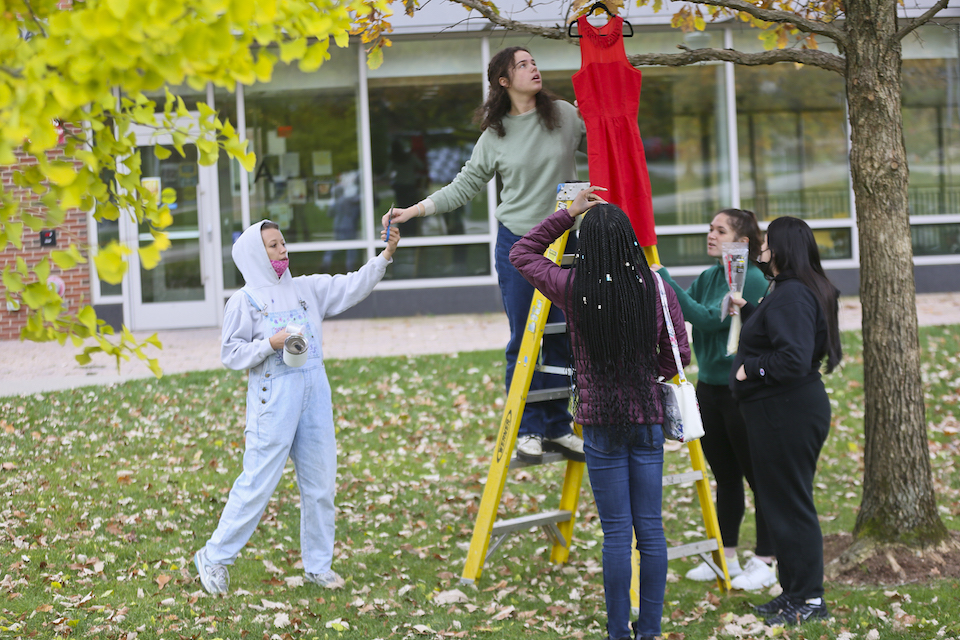 Students hang a red dress on a tree.