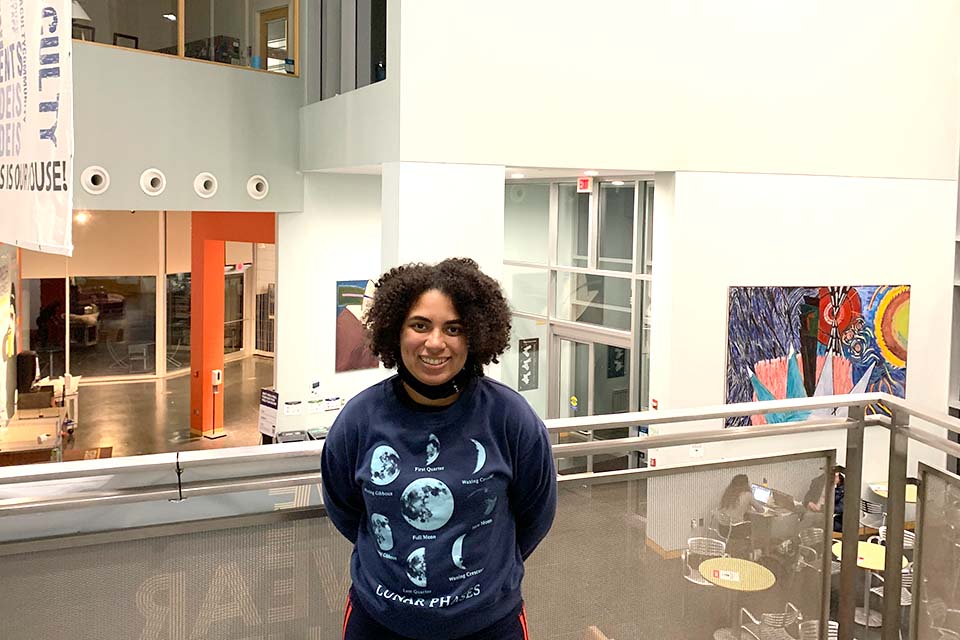 Student Amari Fountain wearing a blue phases of the moon sweatshirt standing on one one of the landings overlooking the SCC.