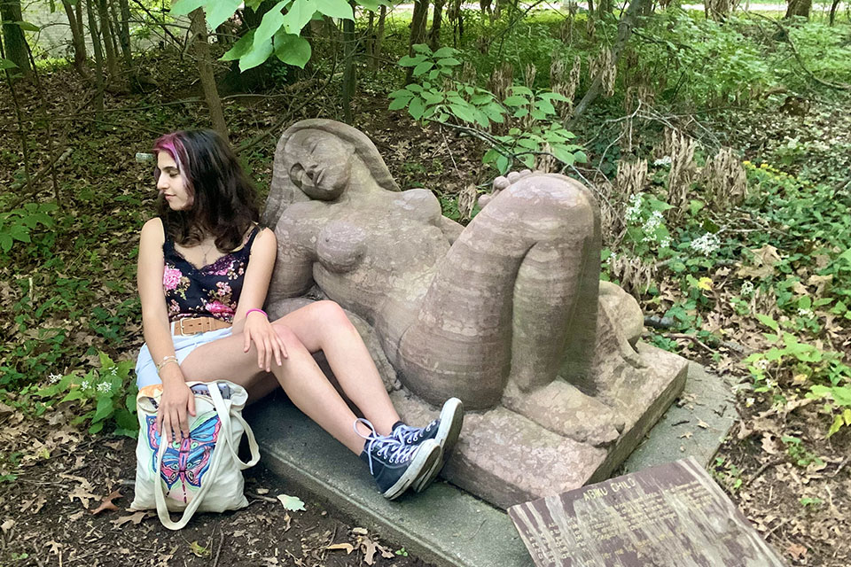 student Natalie Kahn, with pink hair streak, shorts and hightop sneakers, poses with "Sleeping Jennie" a stone statue in a reclining position