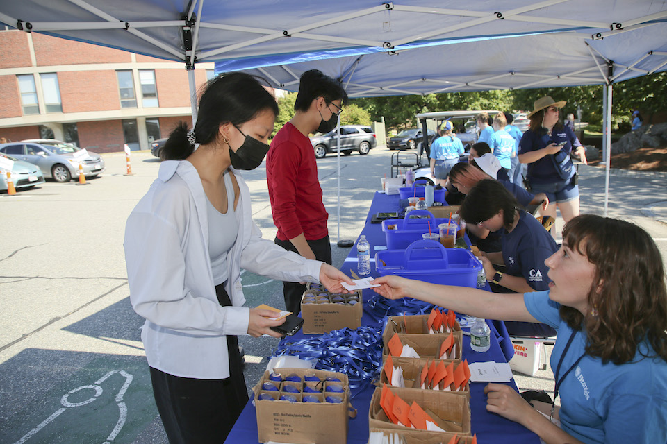 A student gets information from an orientation leader at a tent in the parking lot at orientation