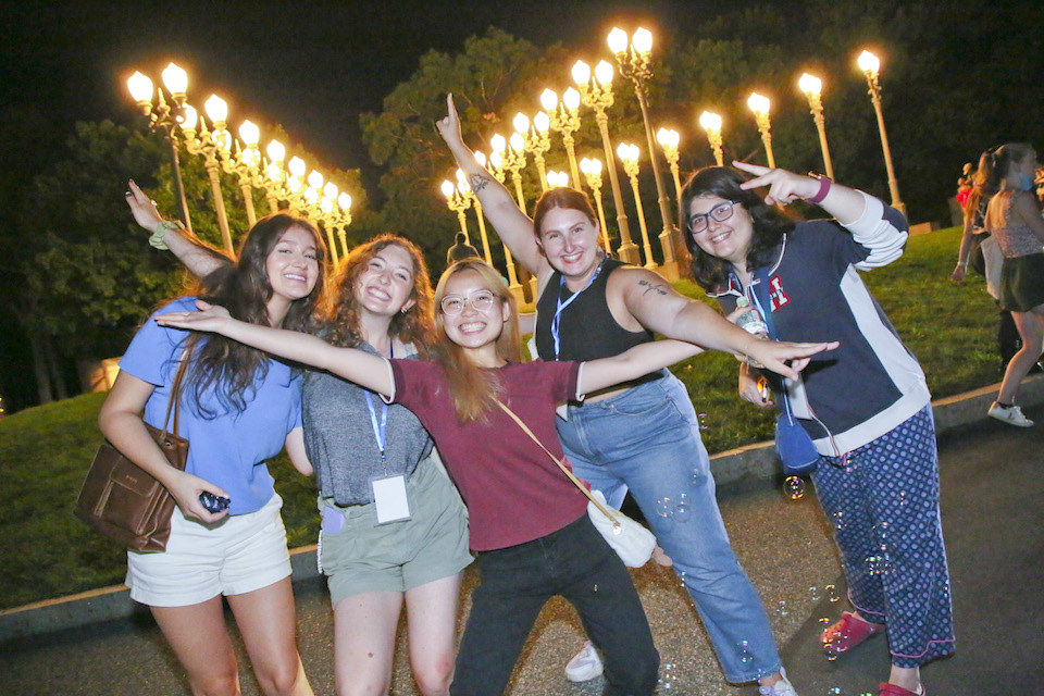 5 students pose for the camera in front of a lit up Light of Reason art installation