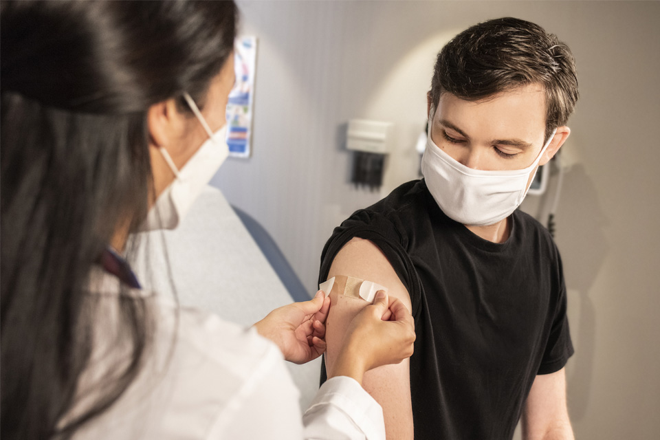 health care provider places a bandage on the arm of a young man as if having just vaccinated him.