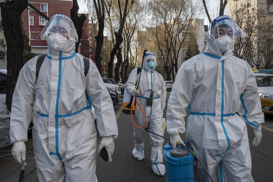 A team of sanitizing workers in hazmat suits walks down a street in china