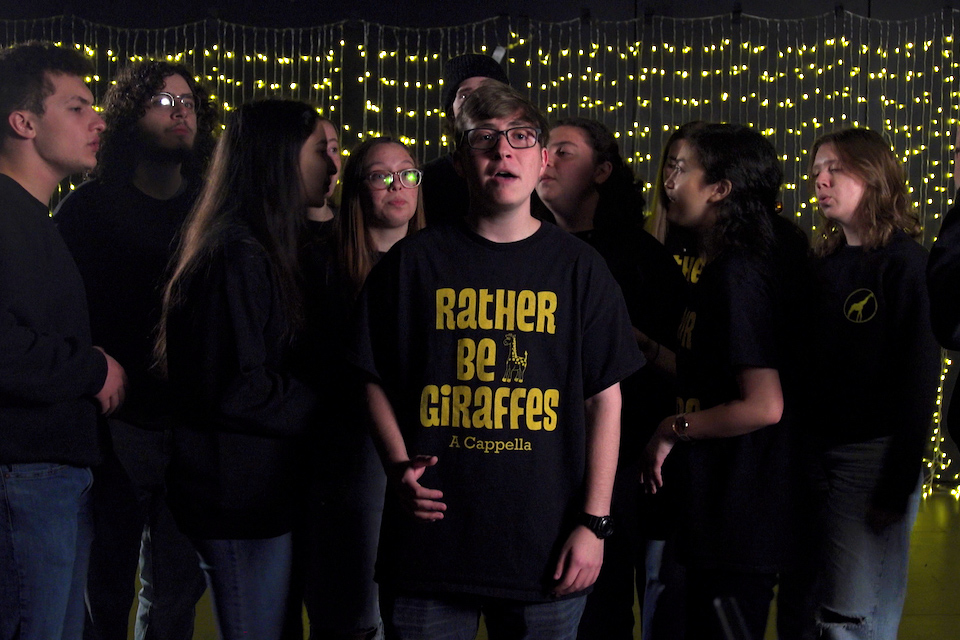 A capella group singing. String lights in background.