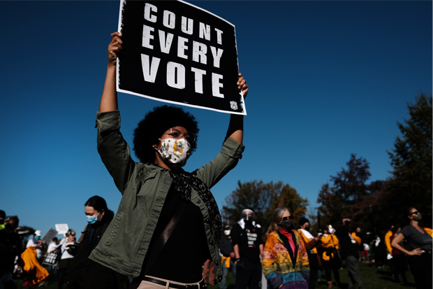 A woman at a protest holds a sign reading "Count Every Vote"