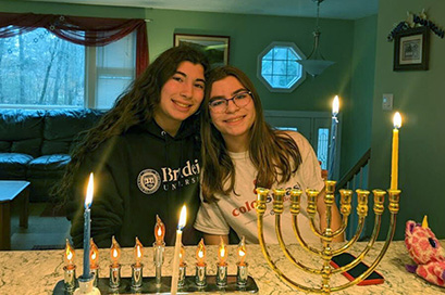 Rachel Finch with her sister standing behind three lit menorahs