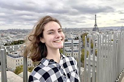 Tasha Epstein with the Eiffel Tower behind her in a wide photo of the Paris skyline