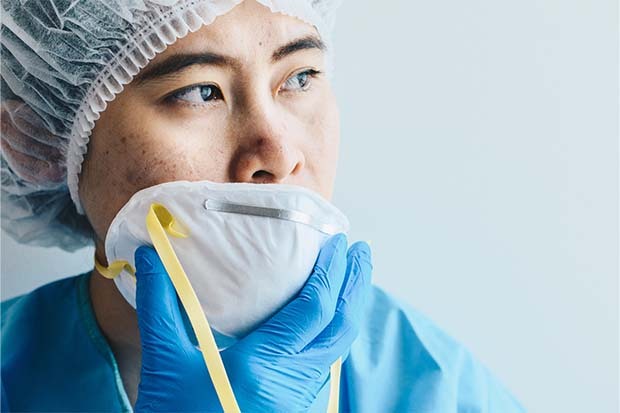 photo of nurse with head covering holding N95 mask over her mouth