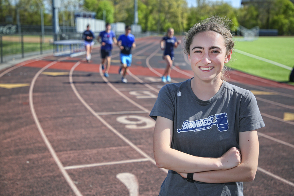 Erin Magil poses on the track with students running behind her